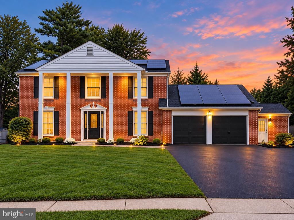 Two-story brick house with white columns, solar panels, and a two-car garage at sunset.