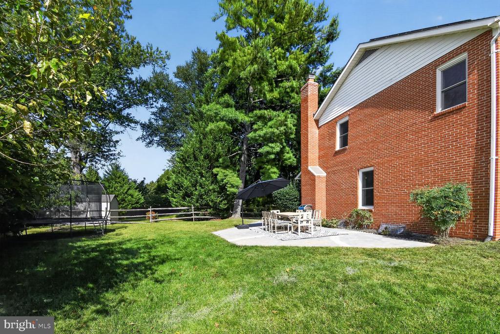 Backyard with a red-brick house, lawn, mature trees, patio dining set, and trampoline.