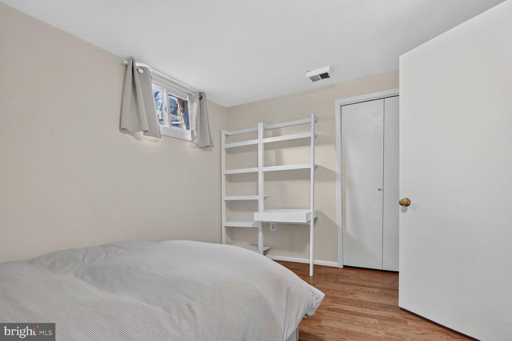 Bedroom with hardwood floors, a curtained window, and white open shelving beside the bed.