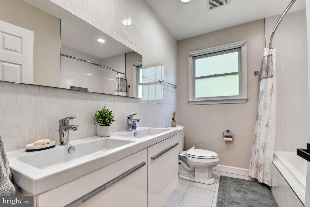 Bathroom with a white double-sink vanity, large mirror, and curtained bathtub.