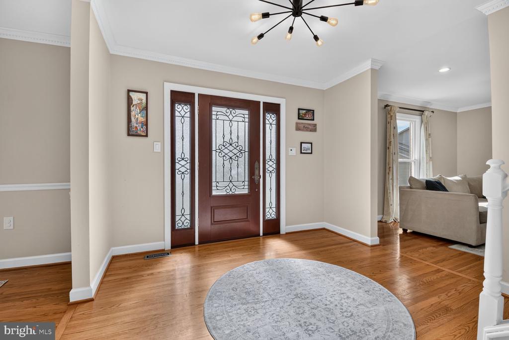 Entry foyer with decorative glass front door, hardwood floors, black chandelier, and round patterned rug.