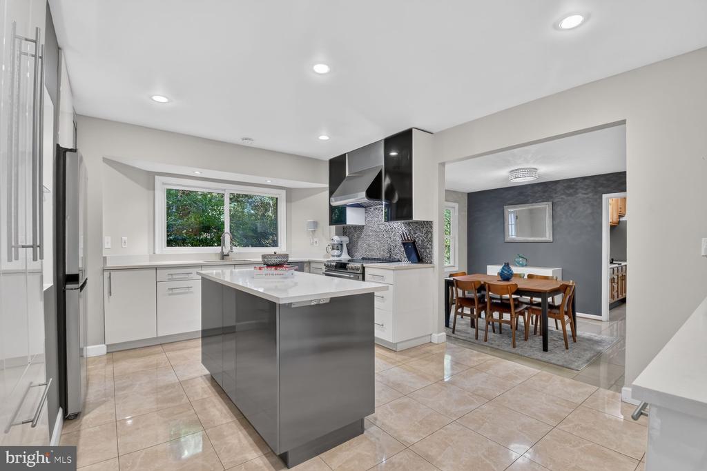 Modern kitchen with a gray island and white cabinets, opening to a dining area.