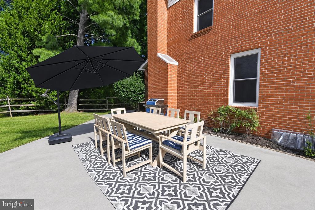 Brick-house patio with a dining set, patterned rug, and large black umbrella.