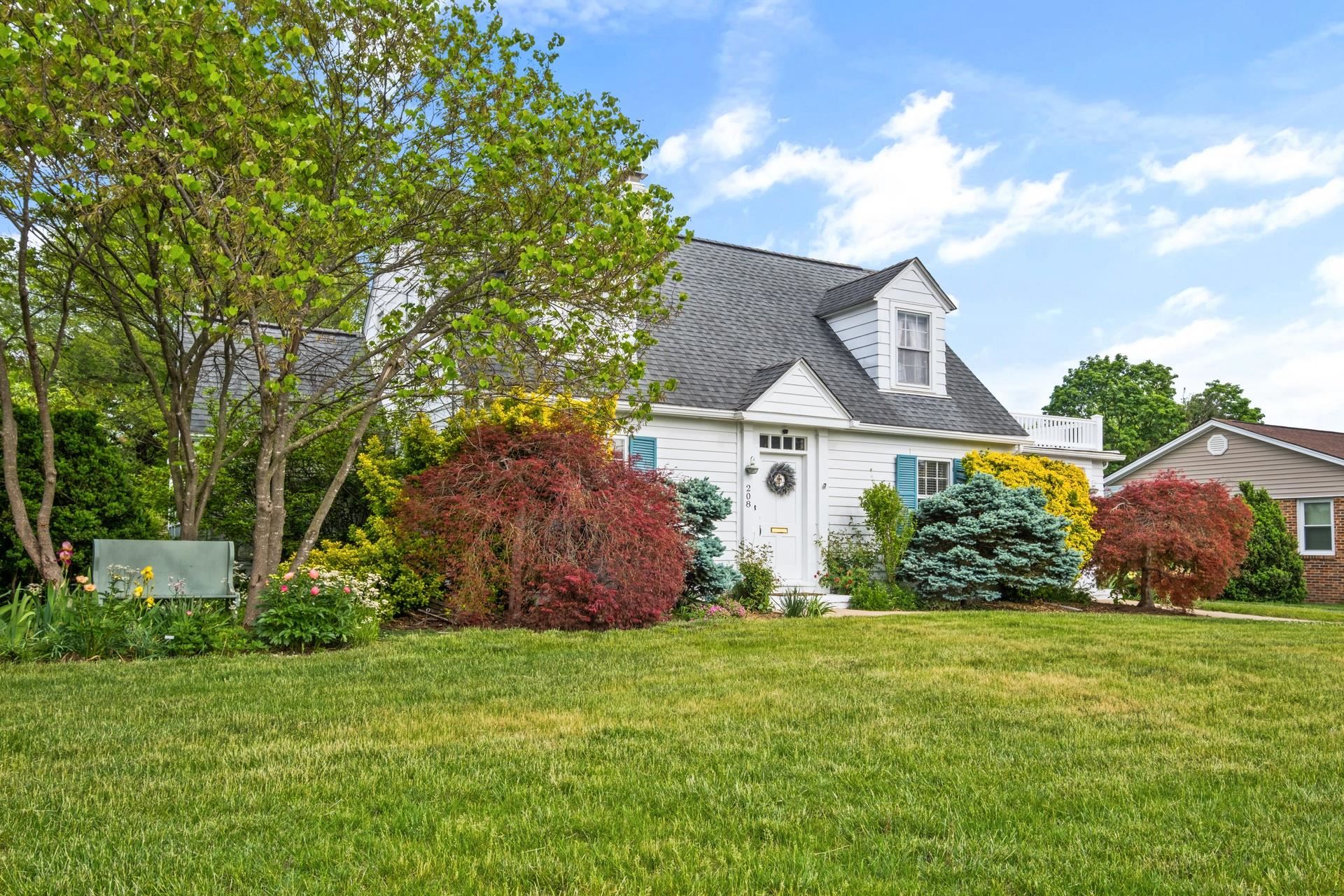 White Cape Cod home with blue shutters, a dormer, and a colorful landscaped garden.