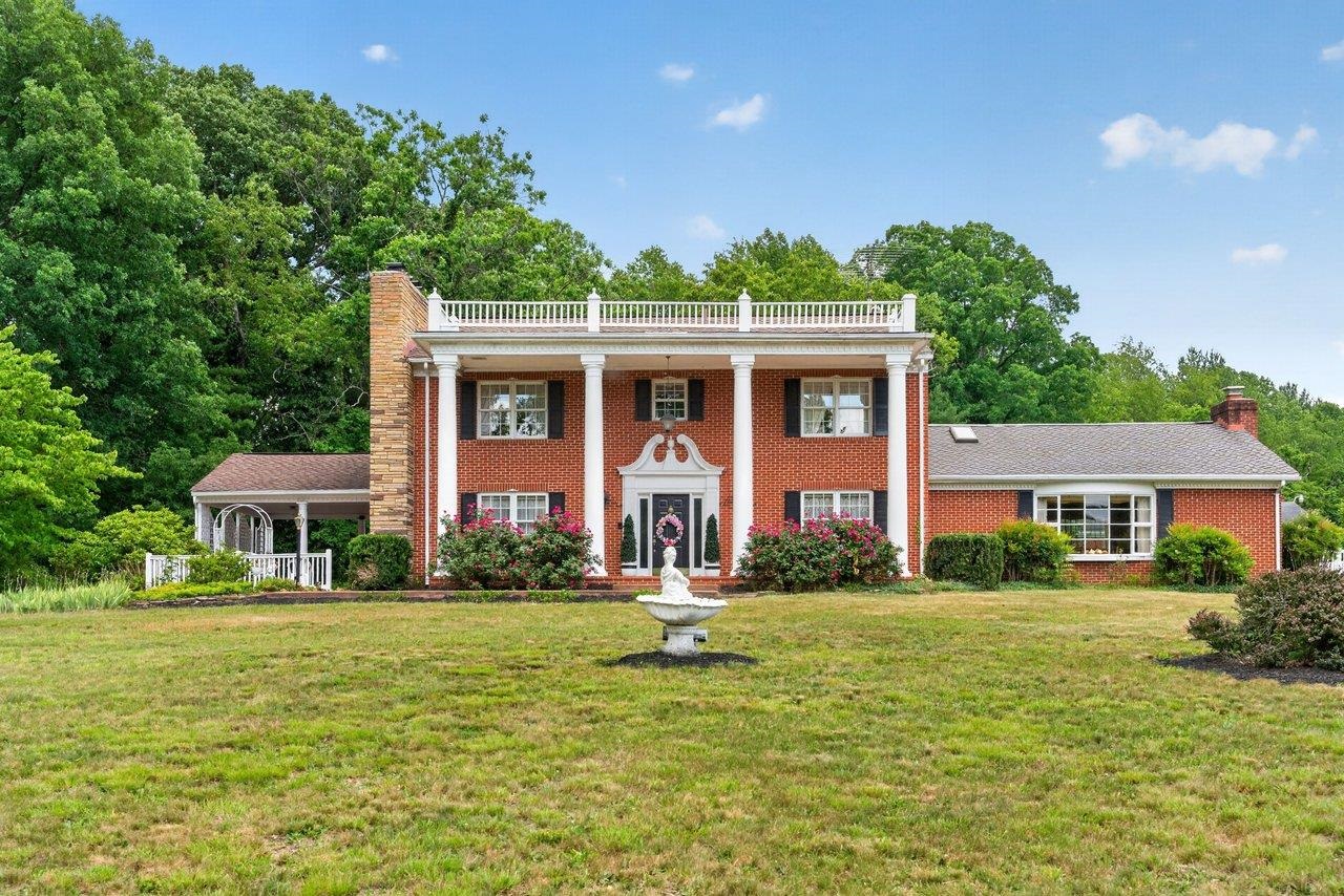 Two-story brick house with white columns, rooftop terrace railing, and a fountain in the front lawn.