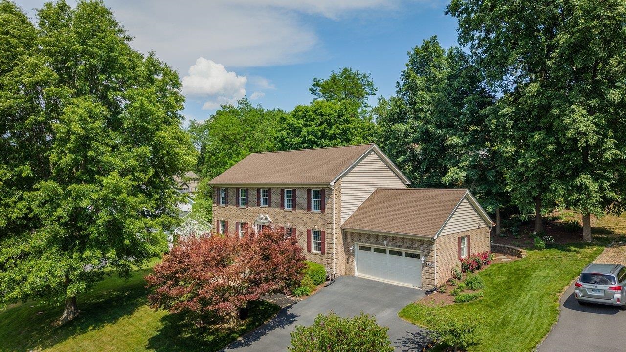 Two-story brick house with an attached garage, mature trees, and landscaped lawn.