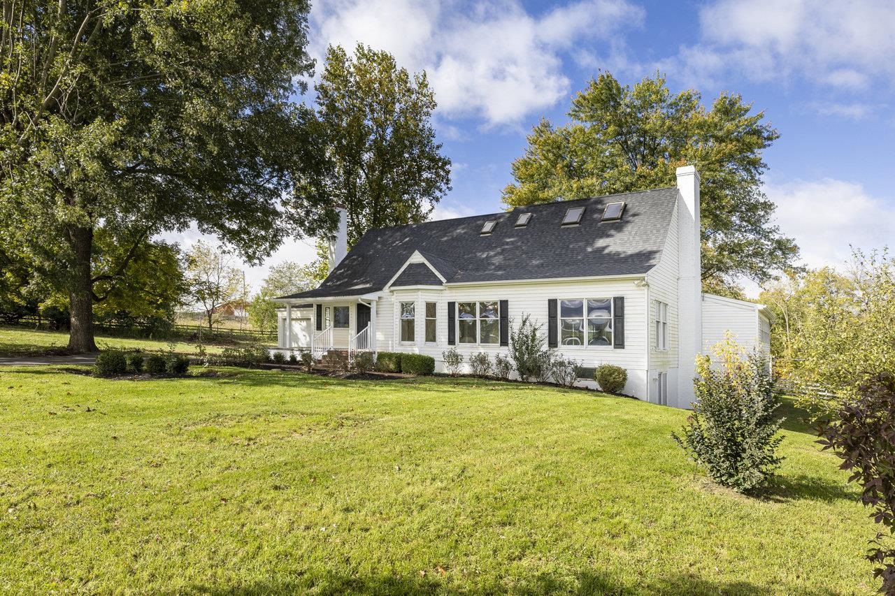 White house with black shutters, skylights, and a covered porch on a broad lawn.