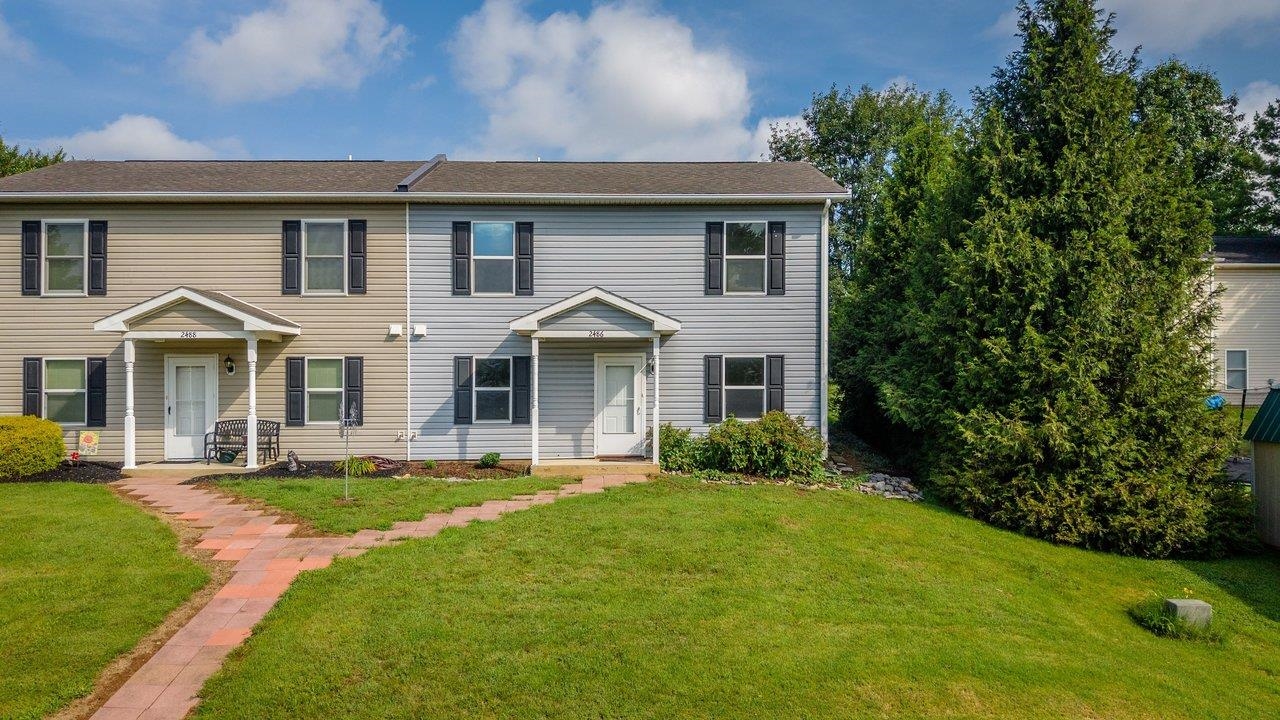 Two attached homes with covered entries and a brick walkway across a green lawn.