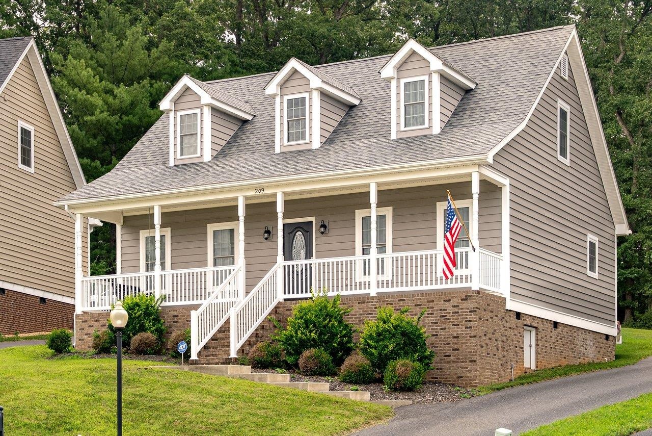 Gray two-story house with brick foundation, white front porch, three dormers, and an American flag.