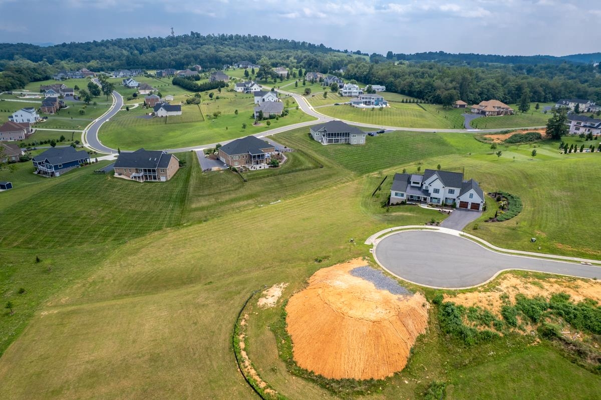 Aerial view of a neighborhood with detached homes, open grassy lots, and a cleared construction site beside a cul-de-sac.