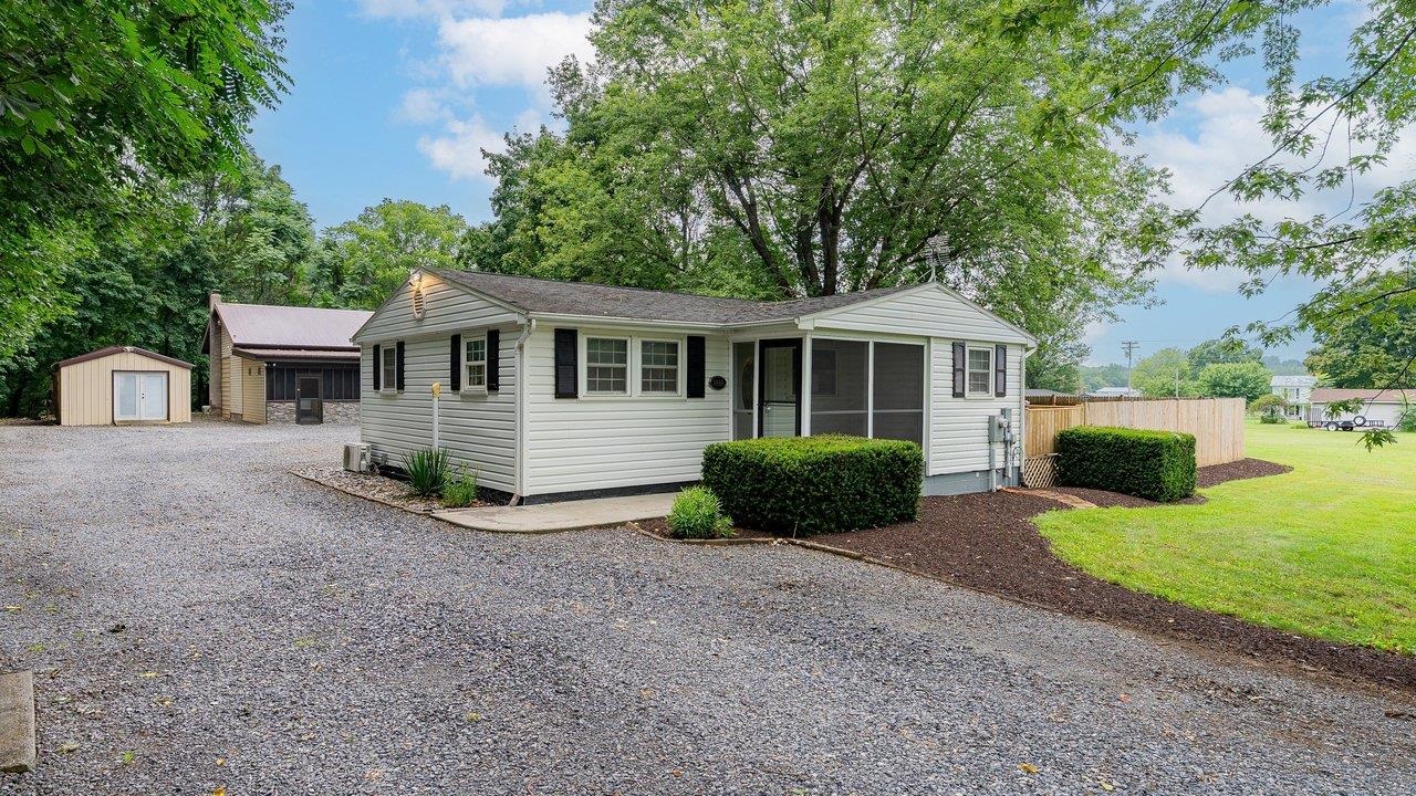 Single-story house with a screened porch, gravel driveway, and two detached outbuildings.