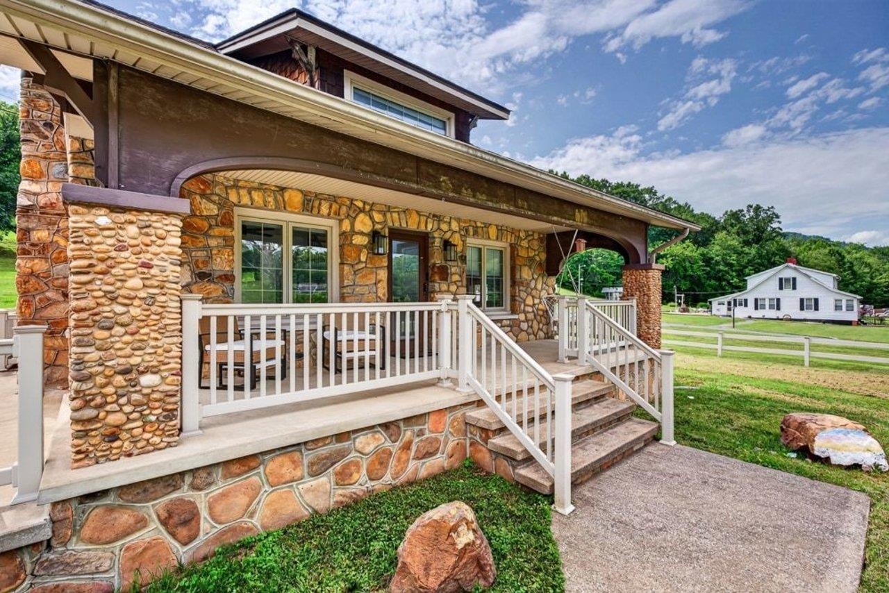 Stone-clad home with a covered porch, white railings, and front steps.