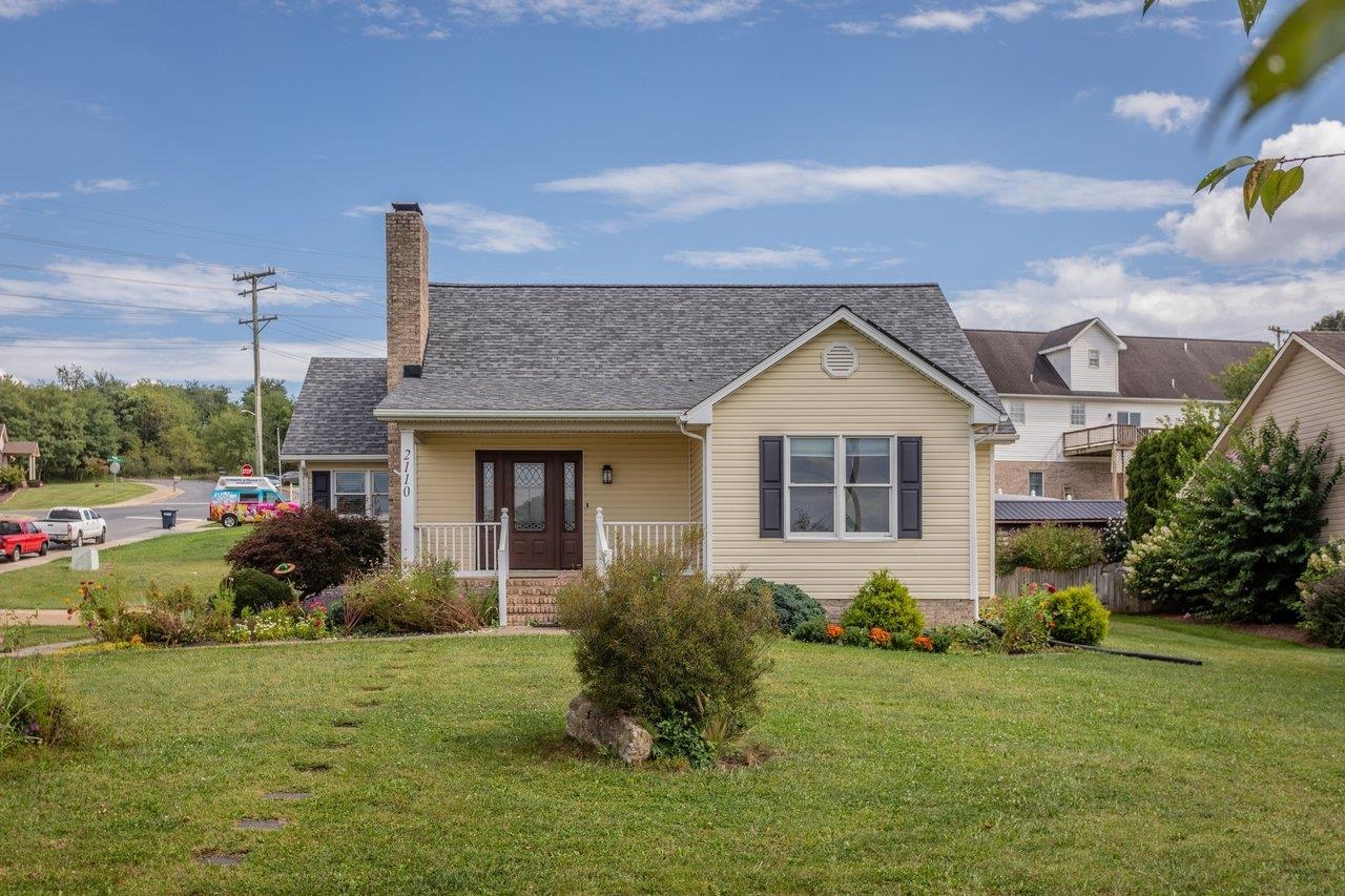Beige house with a brick chimney, covered front porch, and landscaped lawn.