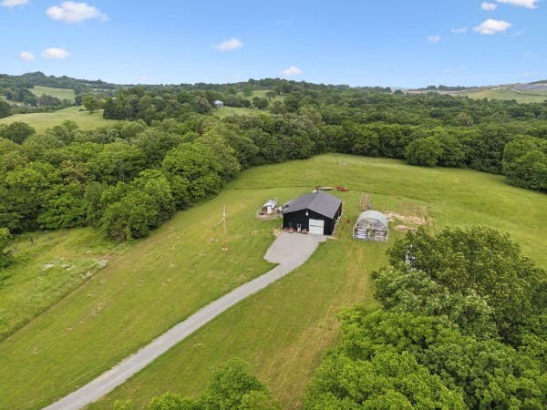 Rural property with a long driveway, dark barn, smaller outbuilding, and wooded hills.