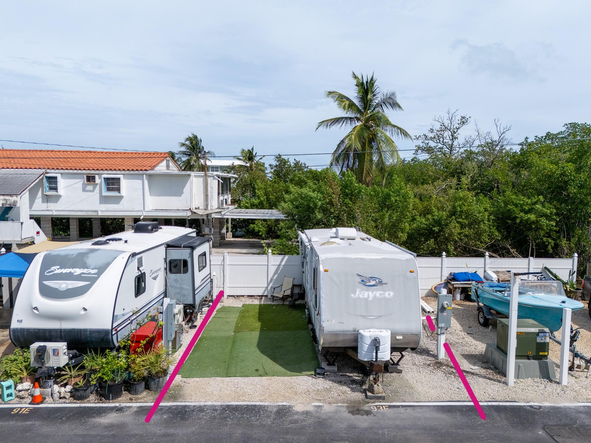 Two RV spaces with travel trailers, a boat, artificial turf, and a raised building behind them.