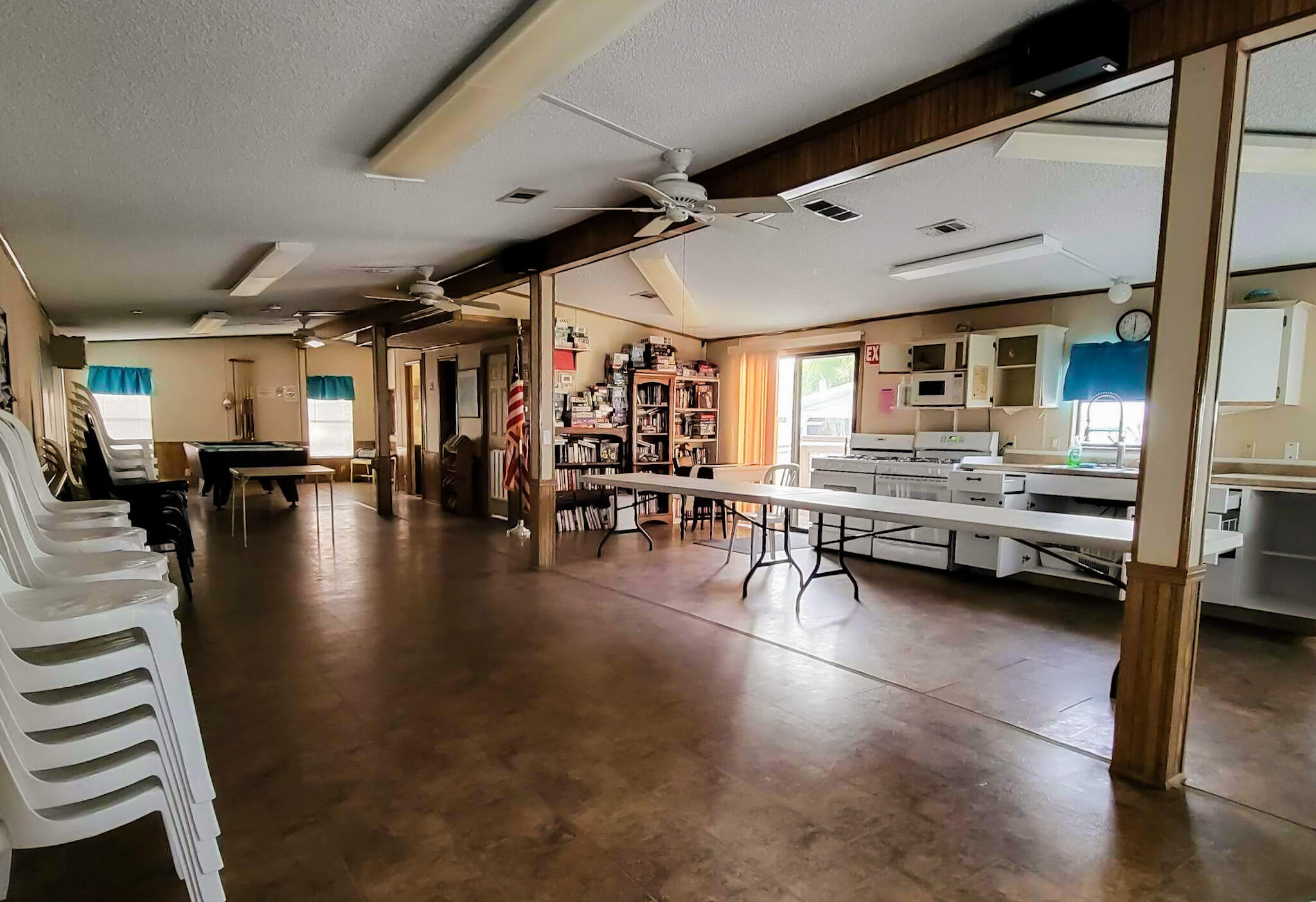 Community room with kitchenette, folding tables, stacked chairs, bookshelves, and a pool table.