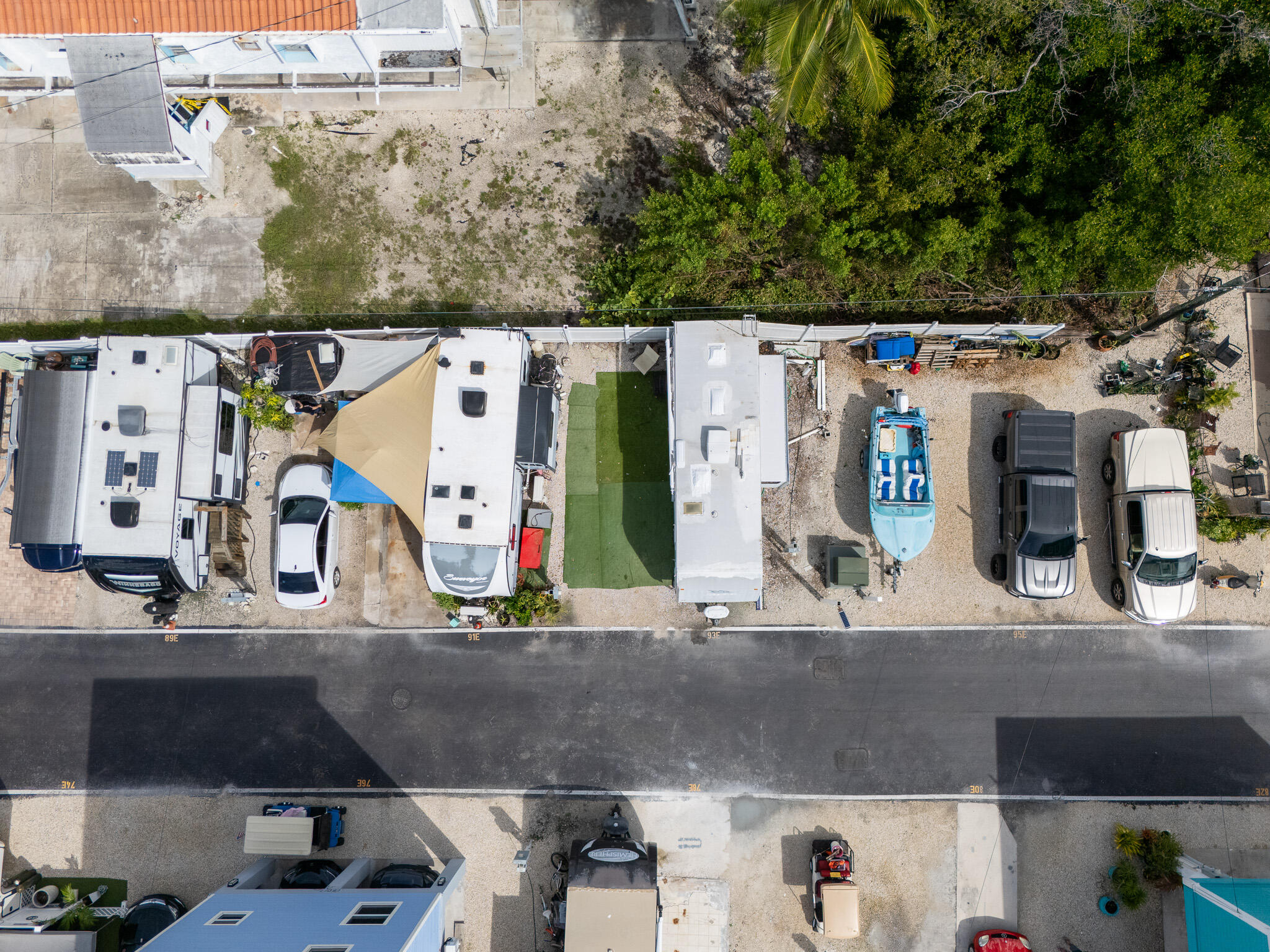 Aerial view of lot 93E with an RV, artificial turf, shade canopy, turquoise boat, and parked vehicles.
