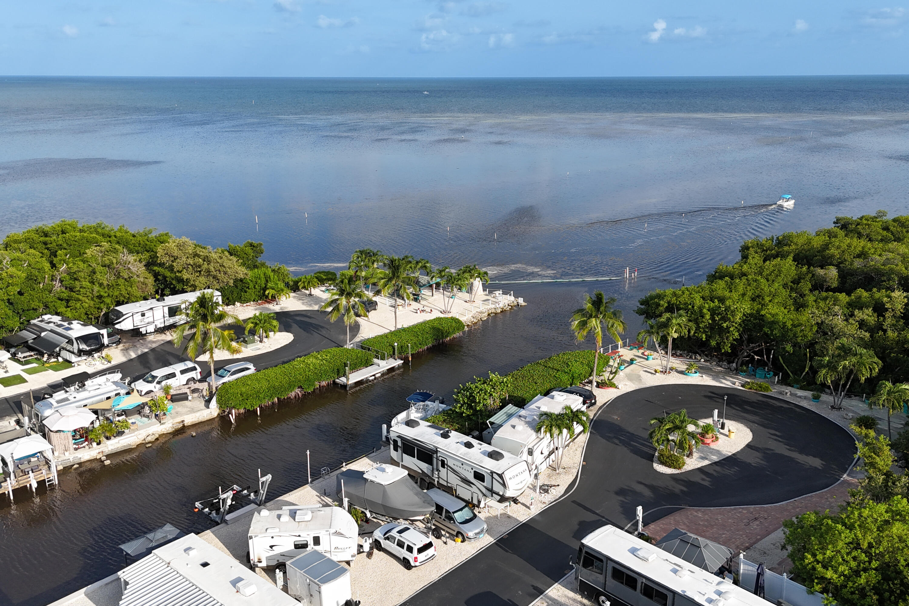 Waterfront RV park with palm-lined sites, a canal, docks, and a boat crossing the bay.