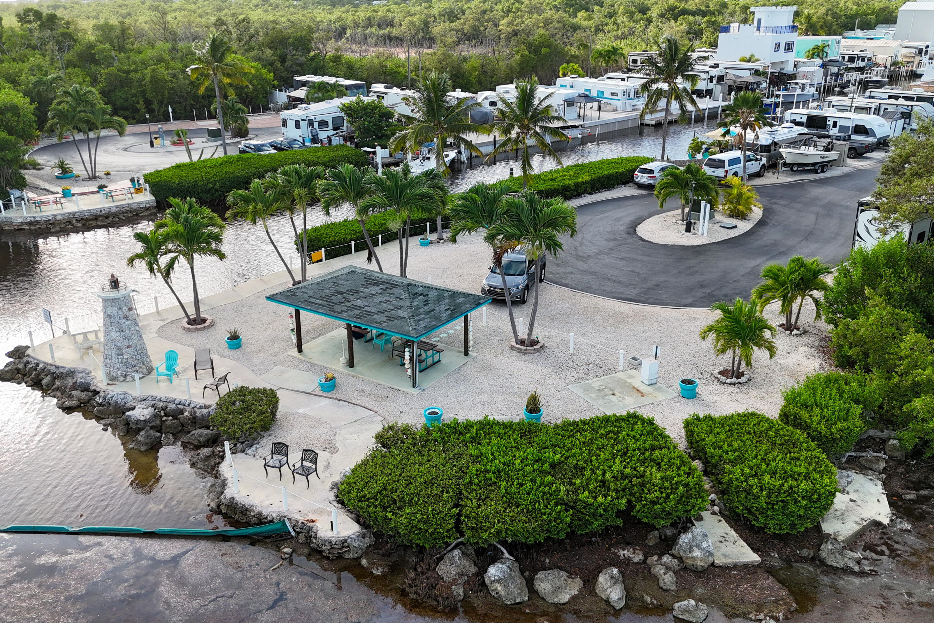 Waterfront marina grounds with a covered pavilion, palm trees, boats, and RVs.