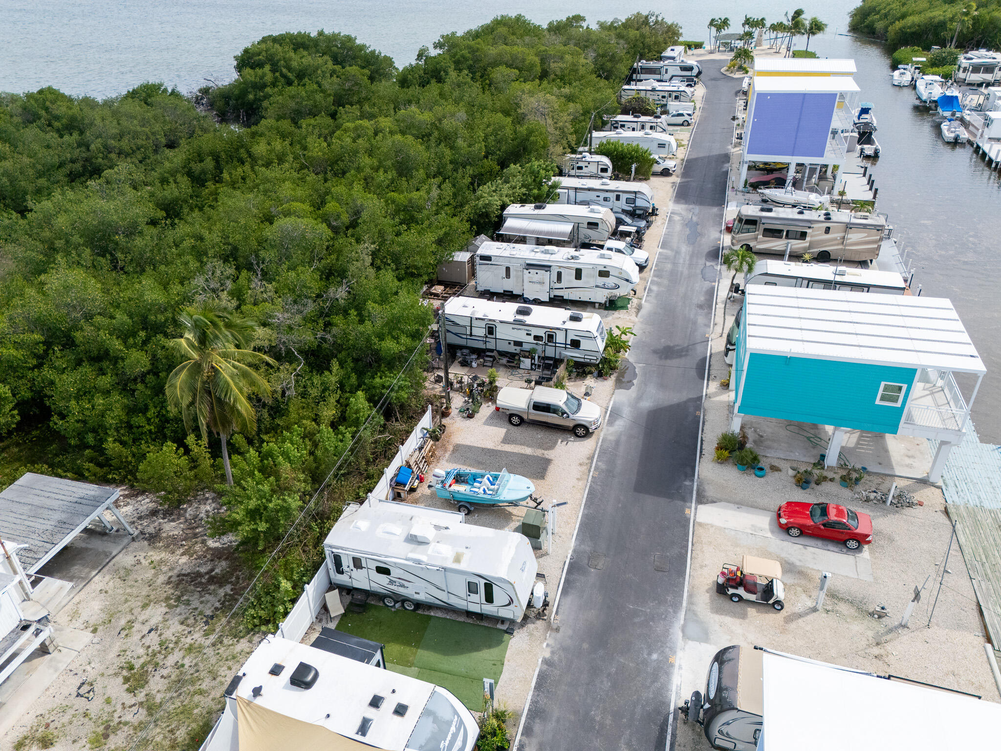 Aerial view of a waterfront RV park with rows of RVs, elevated cottages, boats, and tropical vegetation.