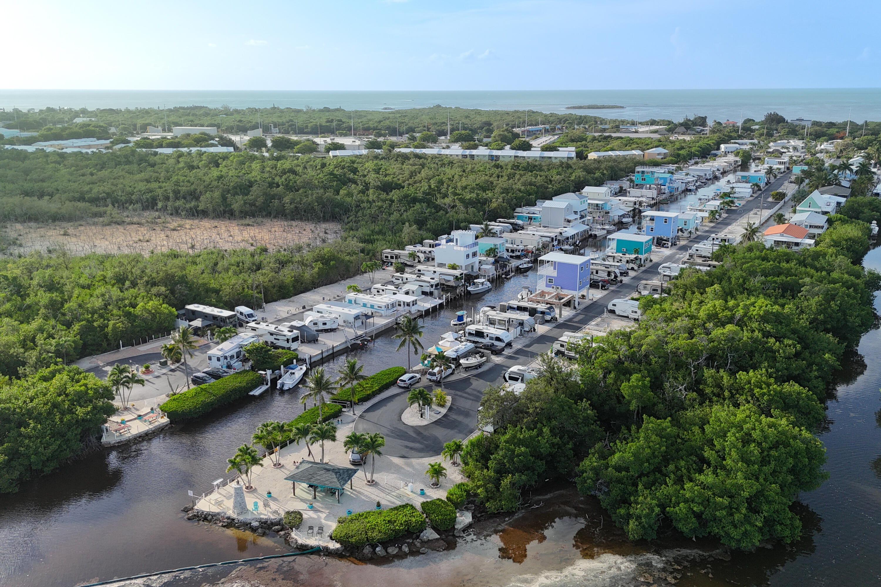 Aerial view of a canal-side community with colorful homes, RVs, mangroves, and ocean beyond.