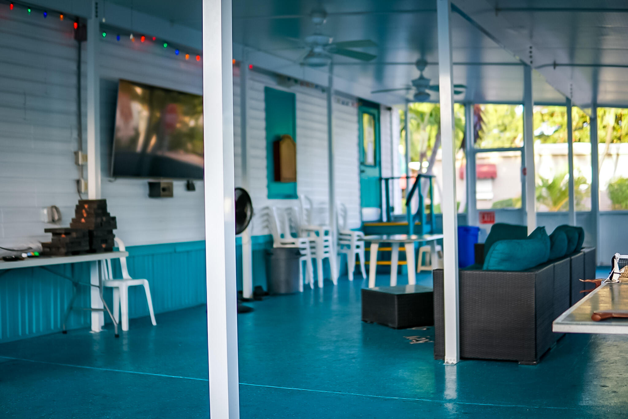 Covered patio with turquoise flooring, ceiling fans, a wall-mounted television, and wicker lounge seating.