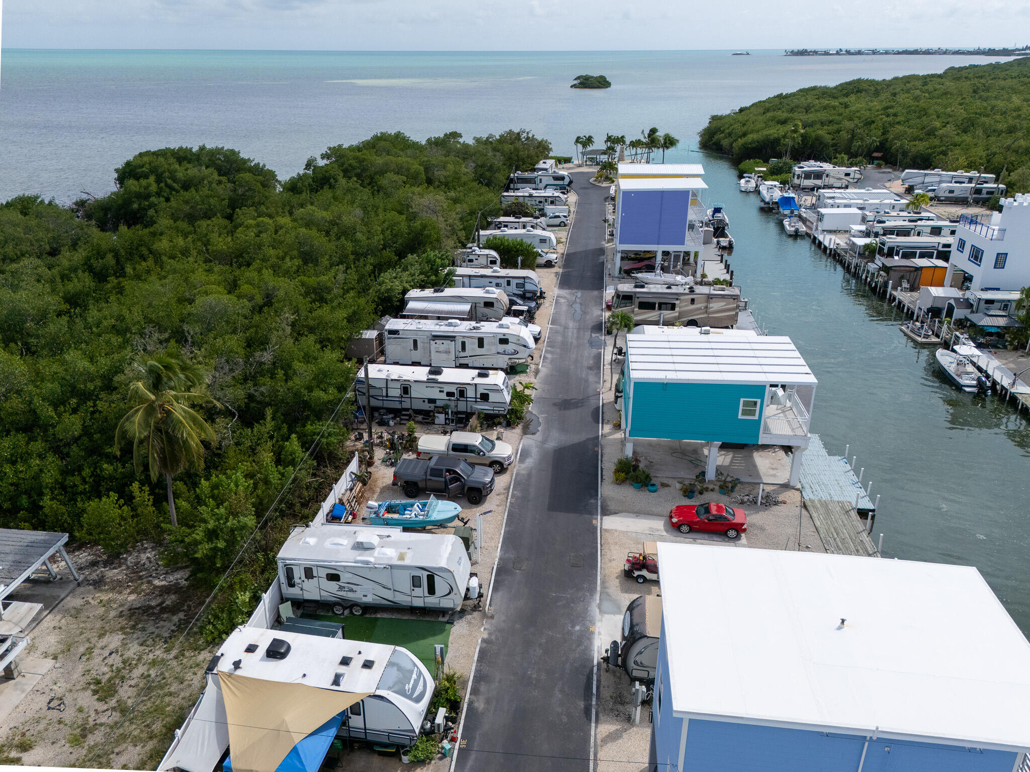 Waterfront RV park with a marina channel, rows of RVs, and an elevated turquoise building.