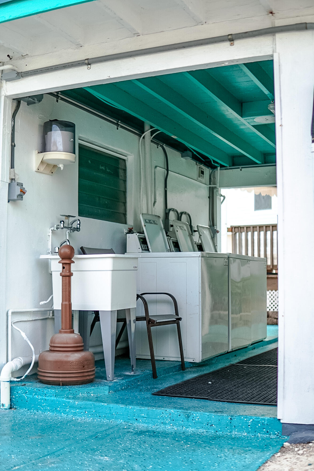 Covered laundry area with large machines, a utility sink, and a turquoise-painted floor and ceiling.
