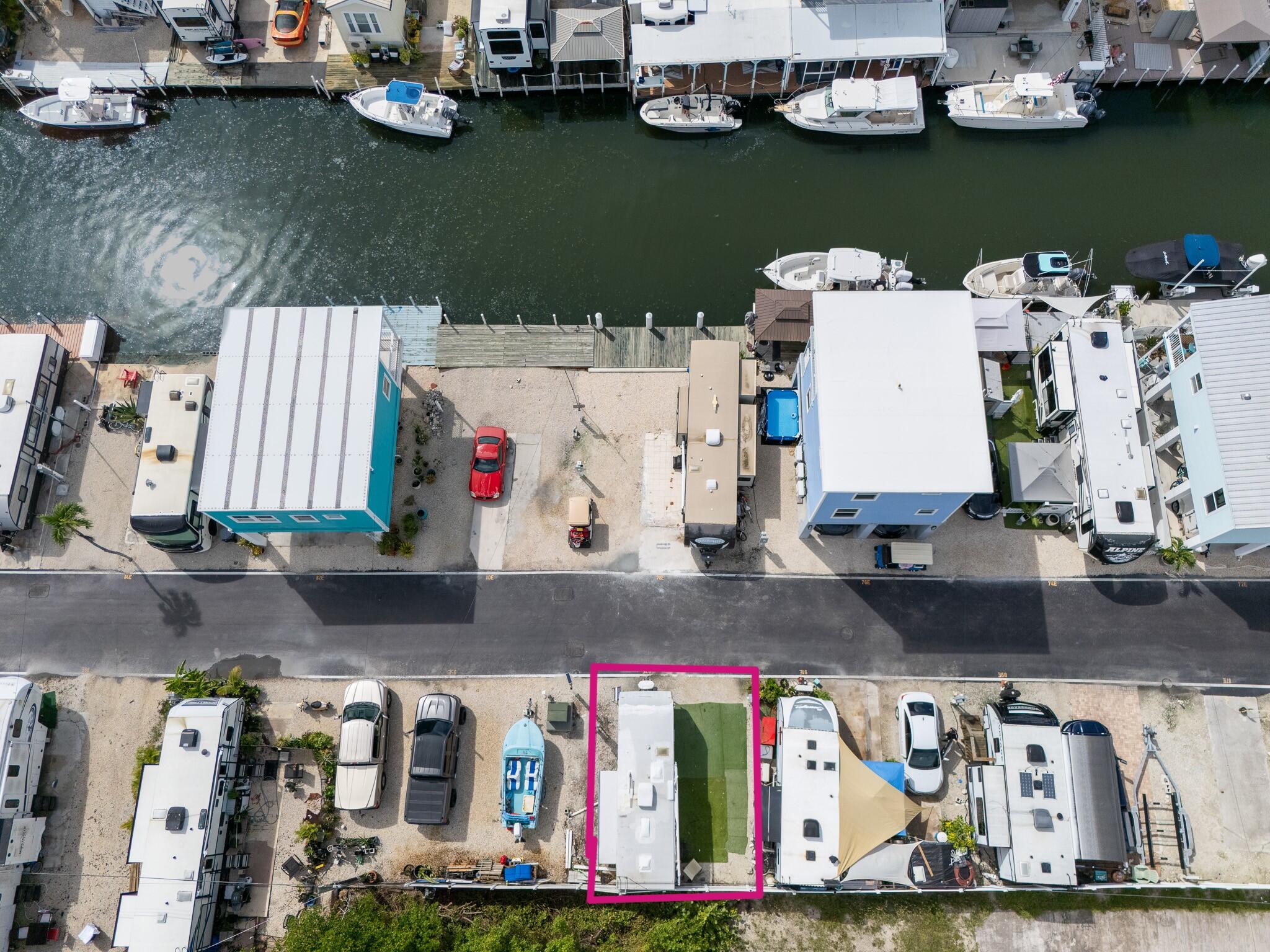 Aerial view of a white mobile home and turf yard on a canal, parcel outlined in magenta.