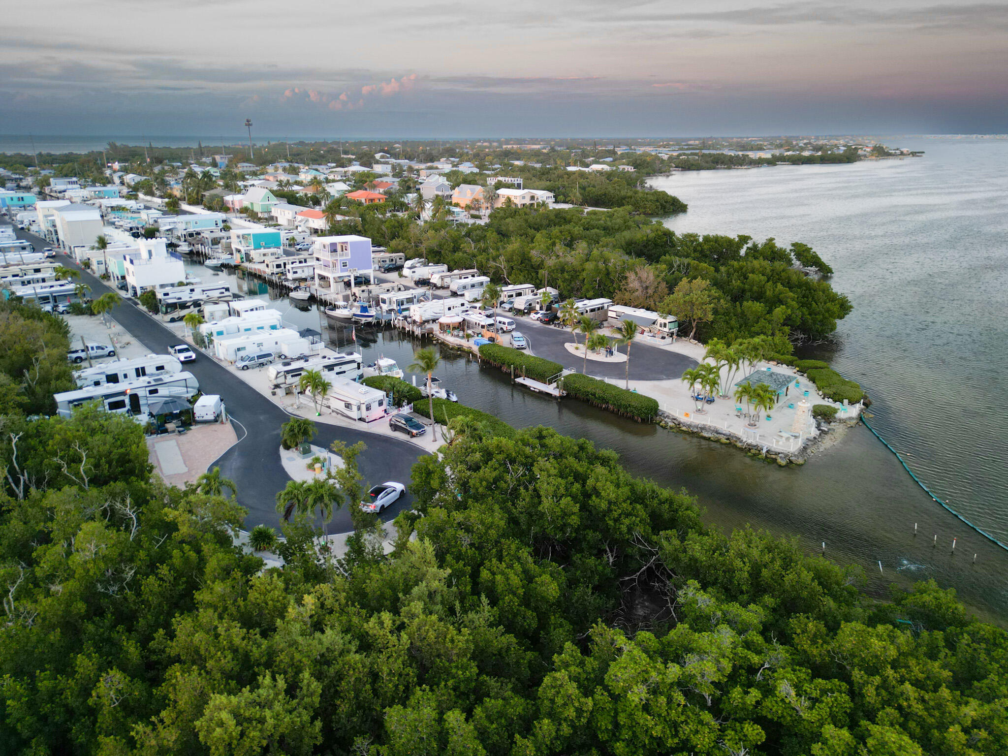 Aerial view of a waterfront RV park with canal slips, palm-lined sites, and surrounding mangroves.