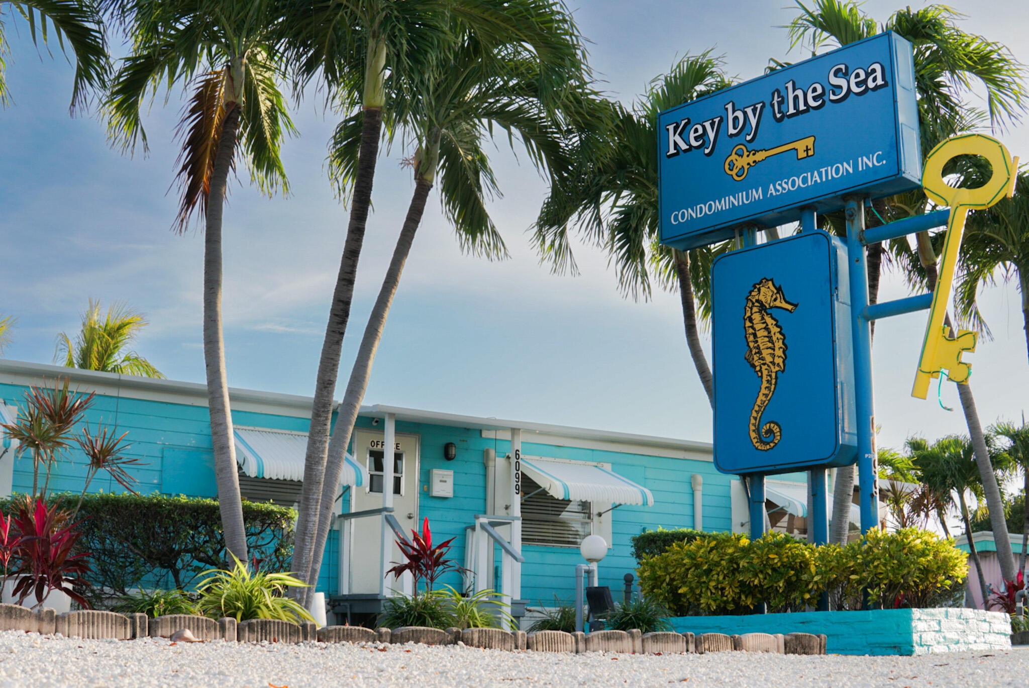 Turquoise Key by the Sea condominium building and blue seahorse sign framed by palm trees.