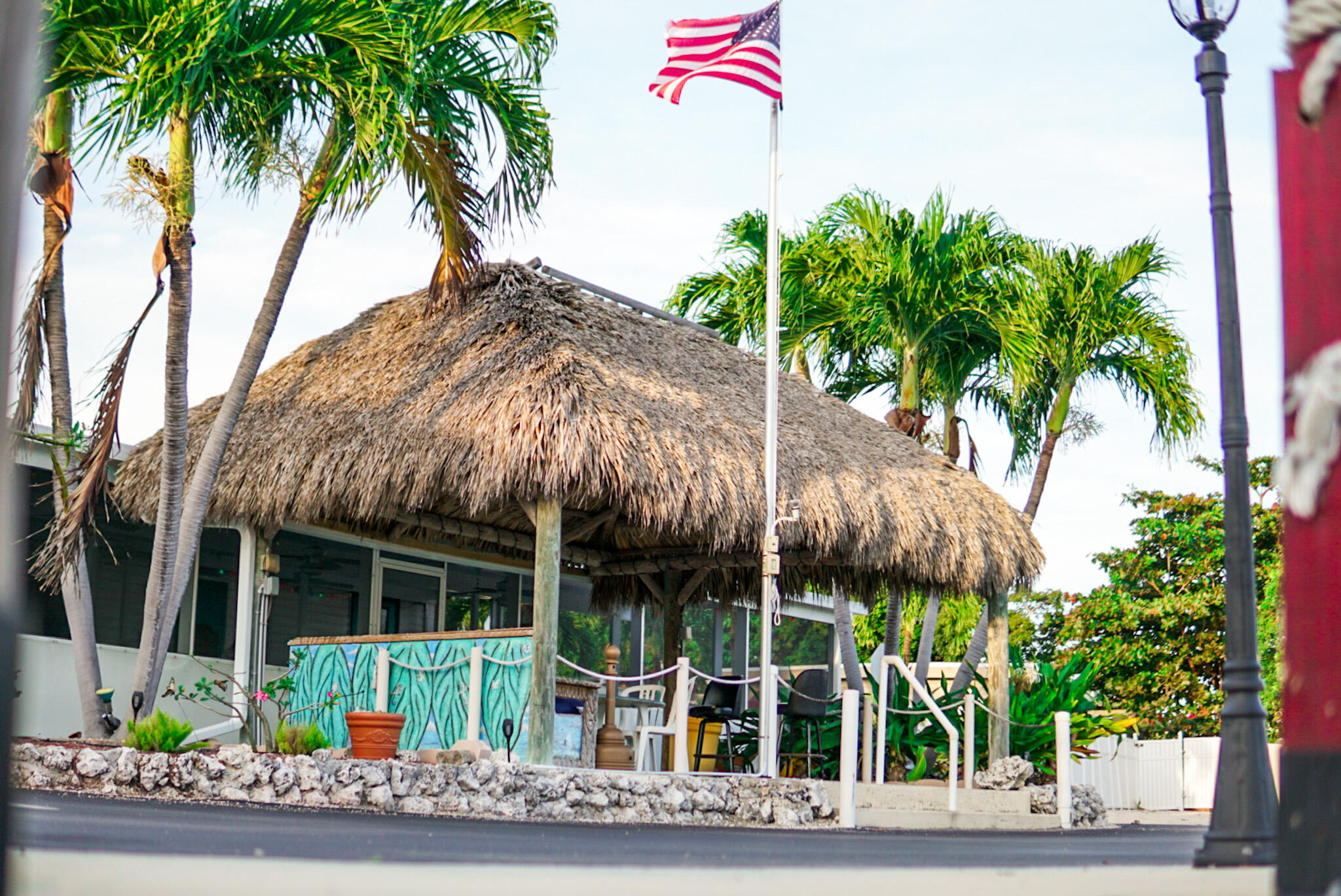 Thatched-roof building with palm trees, outdoor seating, and an American flag.