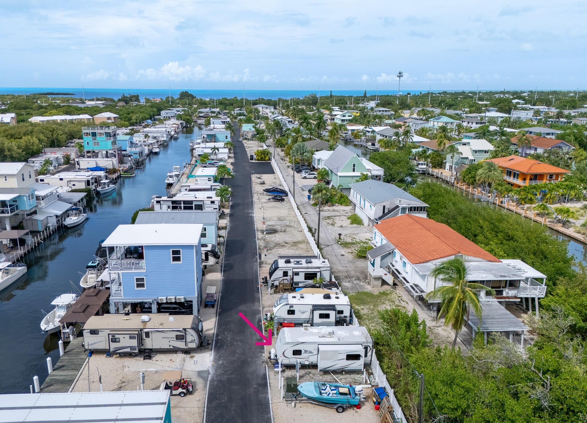 Aerial view of a lot with a travel trailer beside a canal, marked by a pink arrow.