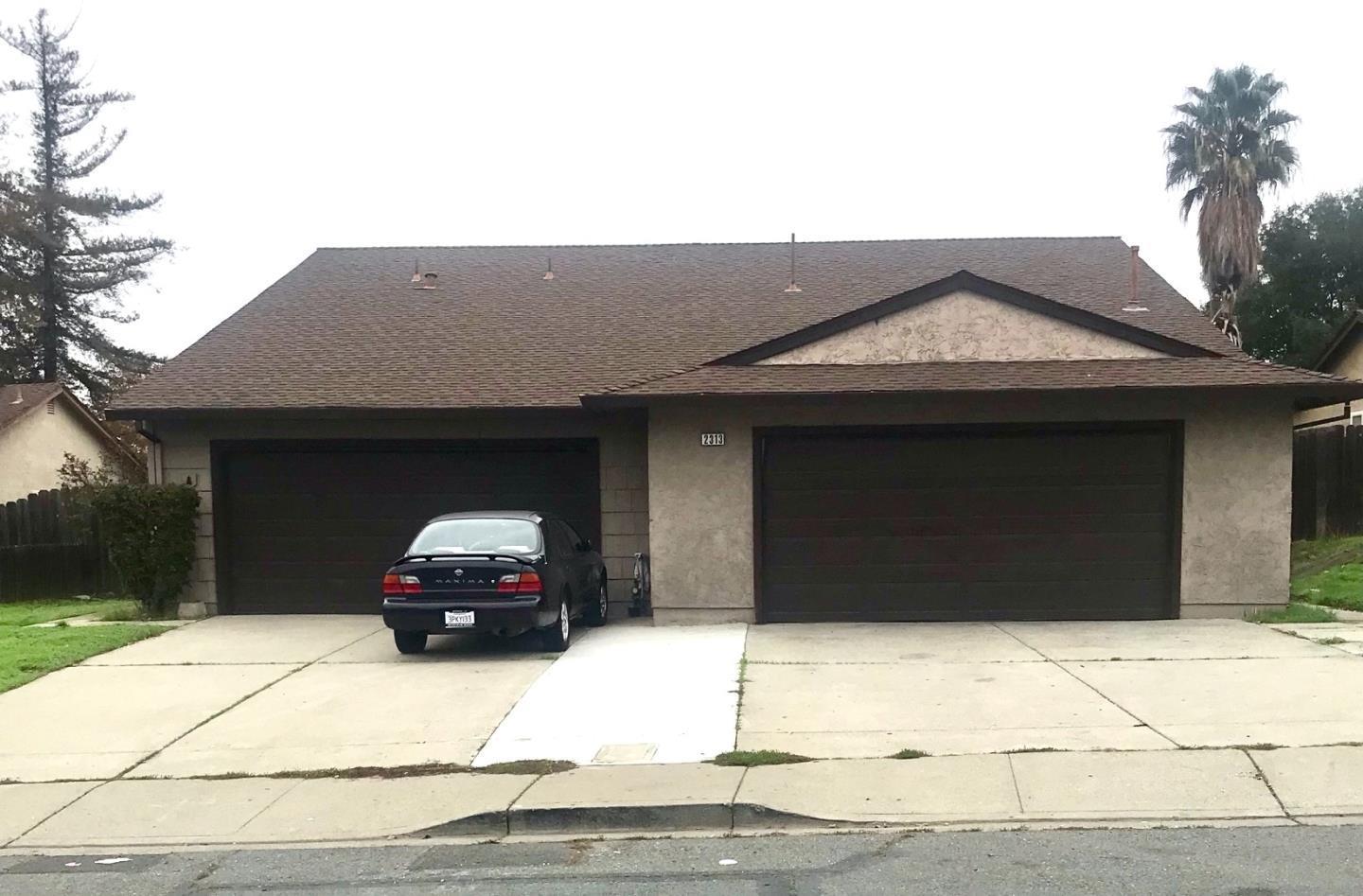 Stucco house with two dark garage doors and a car parked in the driveway.