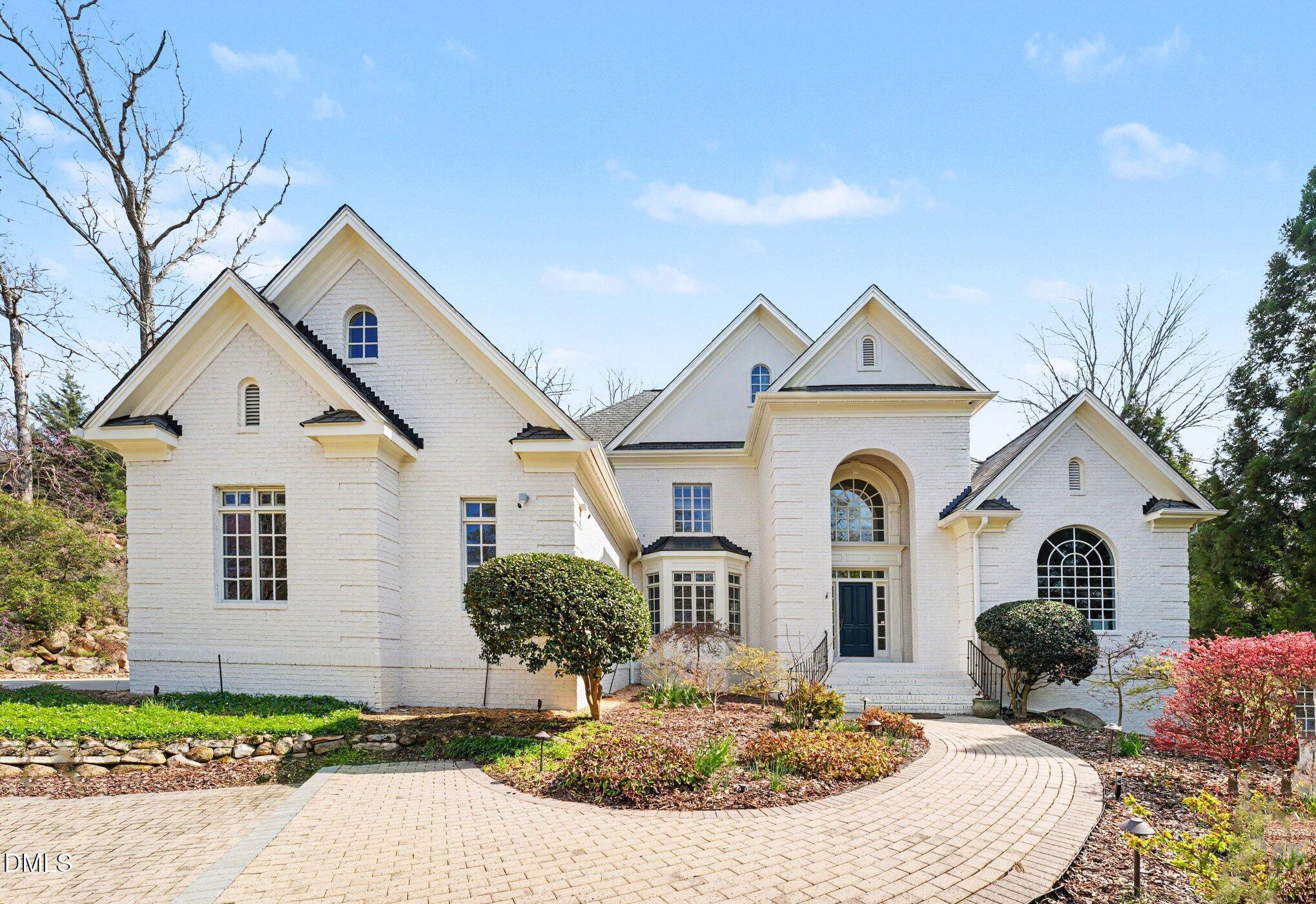 Large white-brick home with multiple gables, an arched entrance, landscaped gardens, and a curved brick driveway.