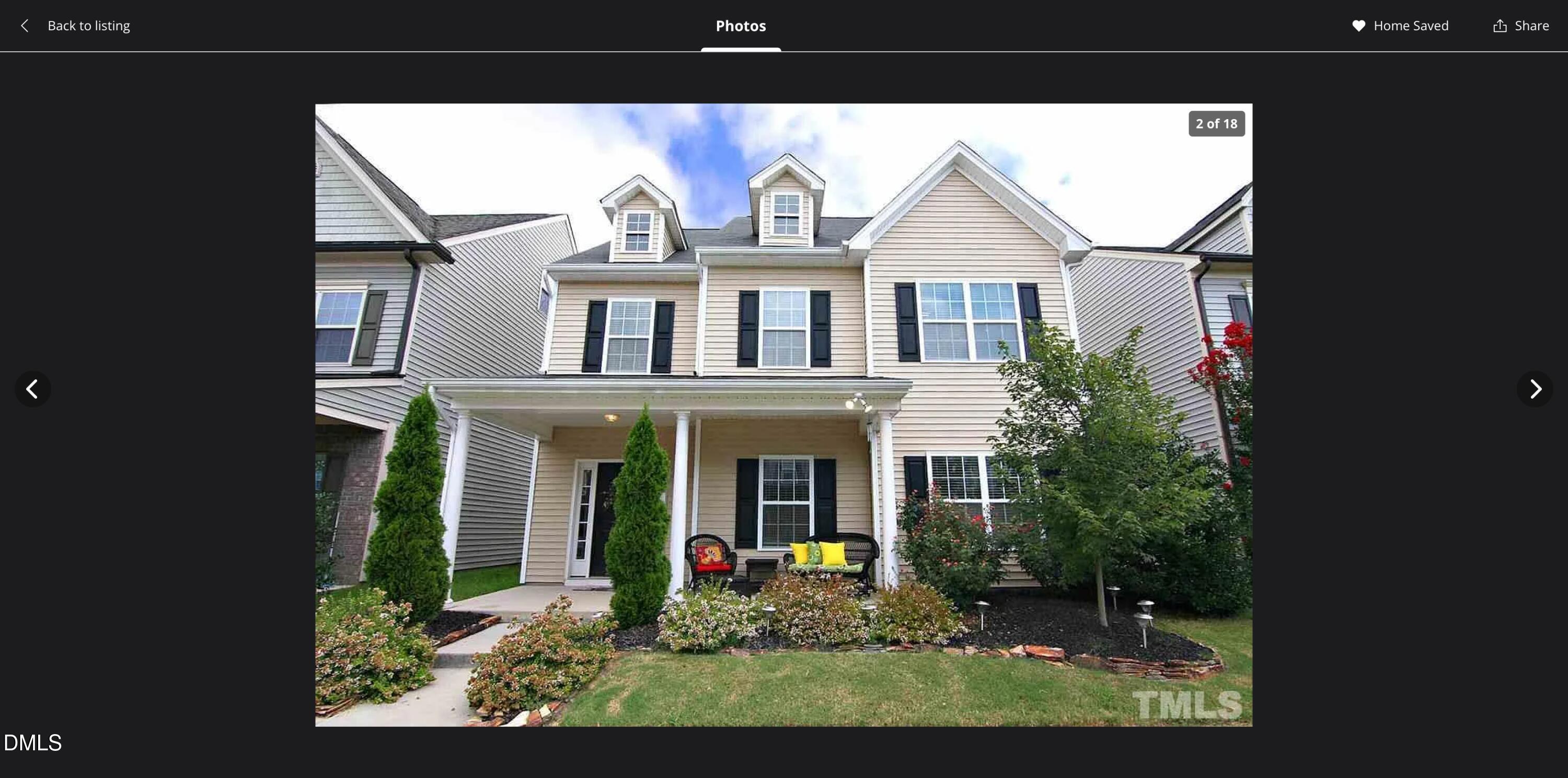 Beige-sided home with a covered porch, black shutters, and landscaped flower beds.
