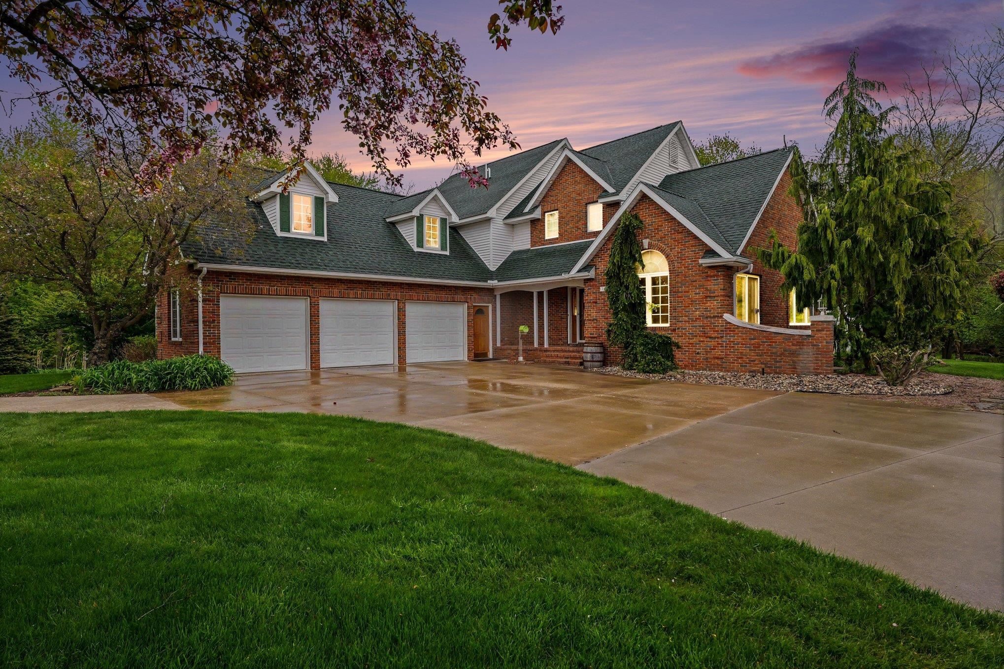 Two-story brick house with a three-car garage and illuminated windows at dusk.