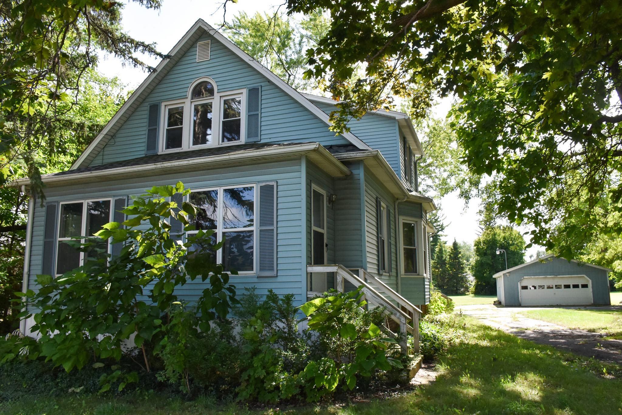 Light blue two-story house with a front gable, leafy trees, and a detached garage.