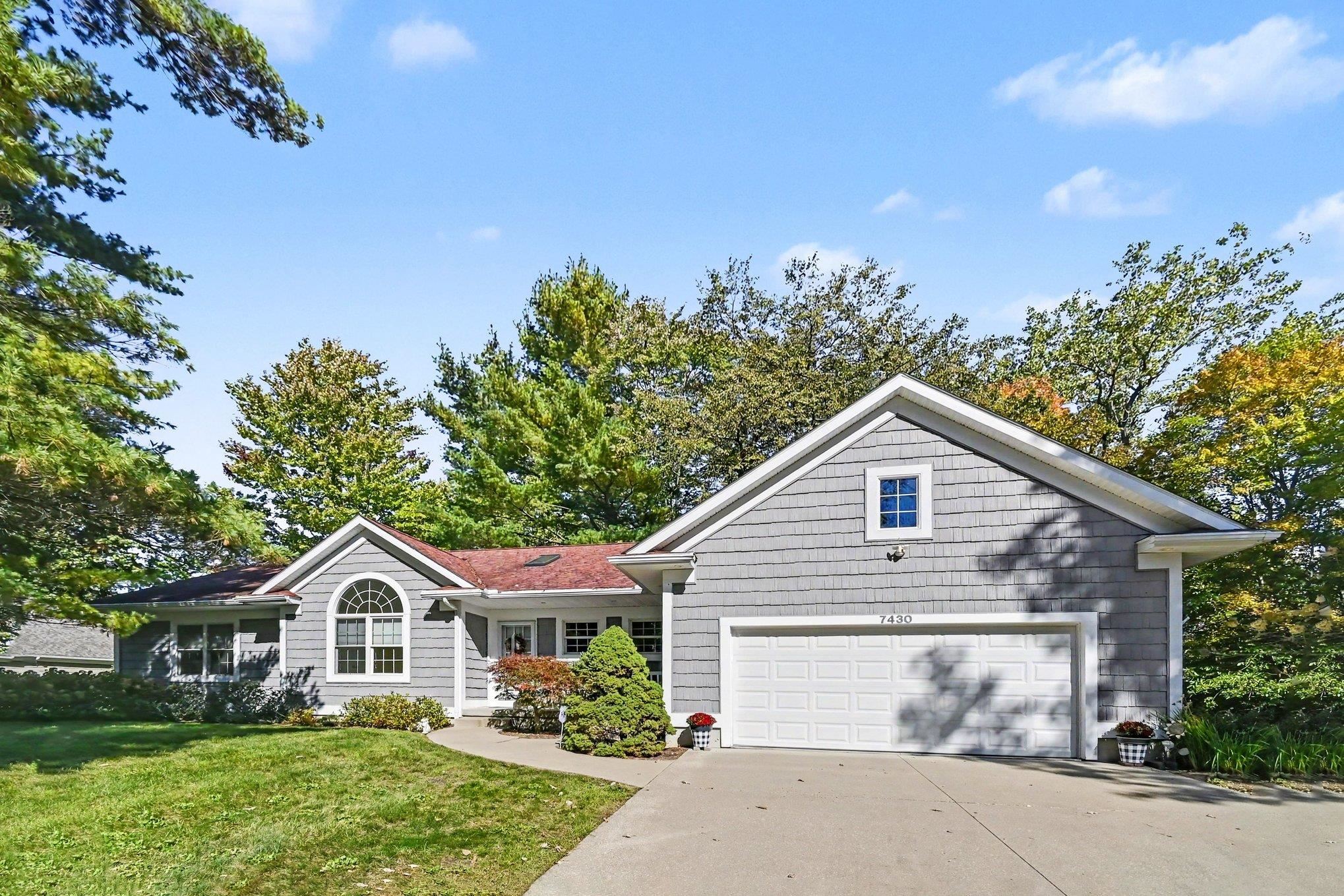 Gray shingle-sided house with a two-car garage, arched window, and mature trees.
