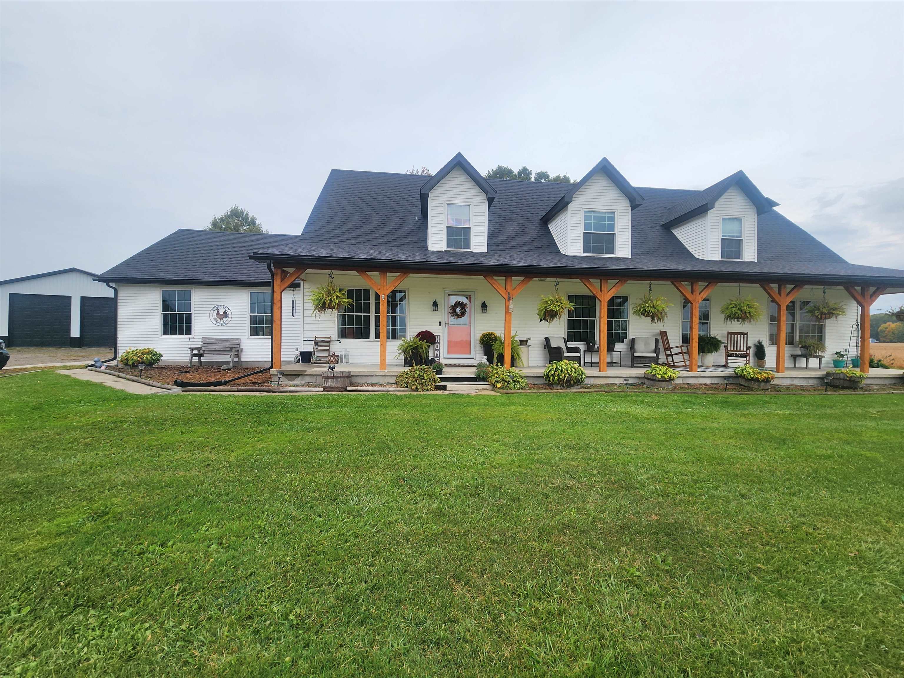 White two-story house with three dormers, a timber-post covered porch, and a broad front lawn.