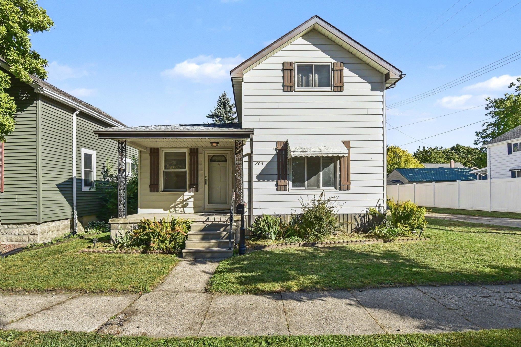 White two-story house with brown shutters, a covered porch, and a small front lawn.