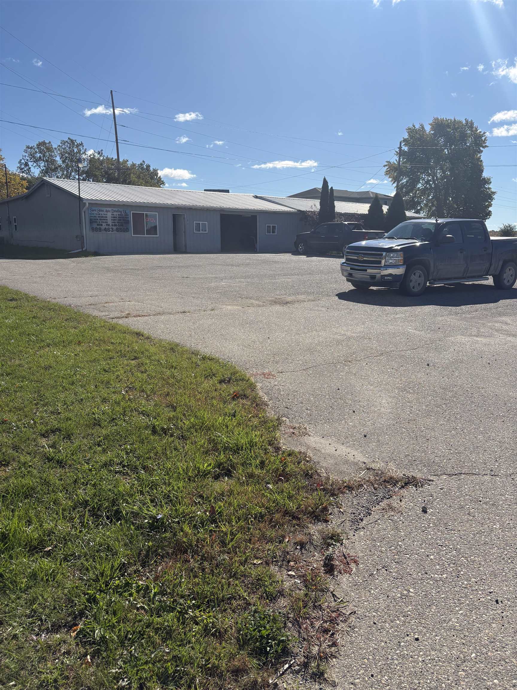 Gray auto detailing shop with a metal roof, garage doors, and pickup trucks in the paved lot.