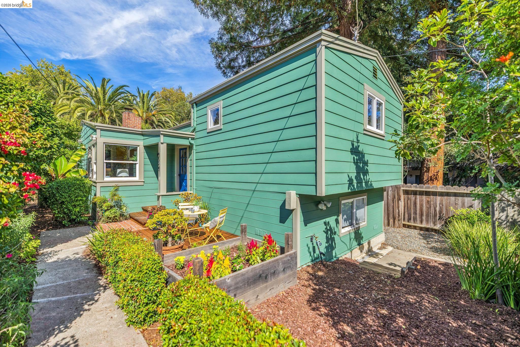 Two-story teal-green house with a small patio and lush garden beds.