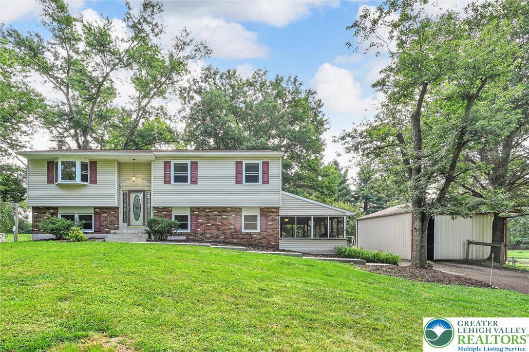 Split-level house with white siding, brick lower level, enclosed porch, and detached outbuilding.