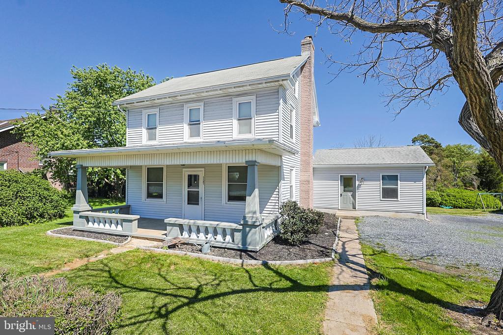 White two-story house with a covered porch, one-story side wing, and gravel driveway.