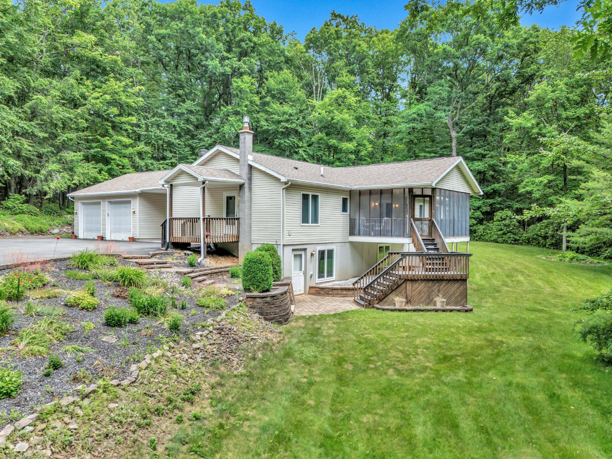 Light-colored home with a two-car garage, screened porch, and multi-level decks amid trees and lawn.