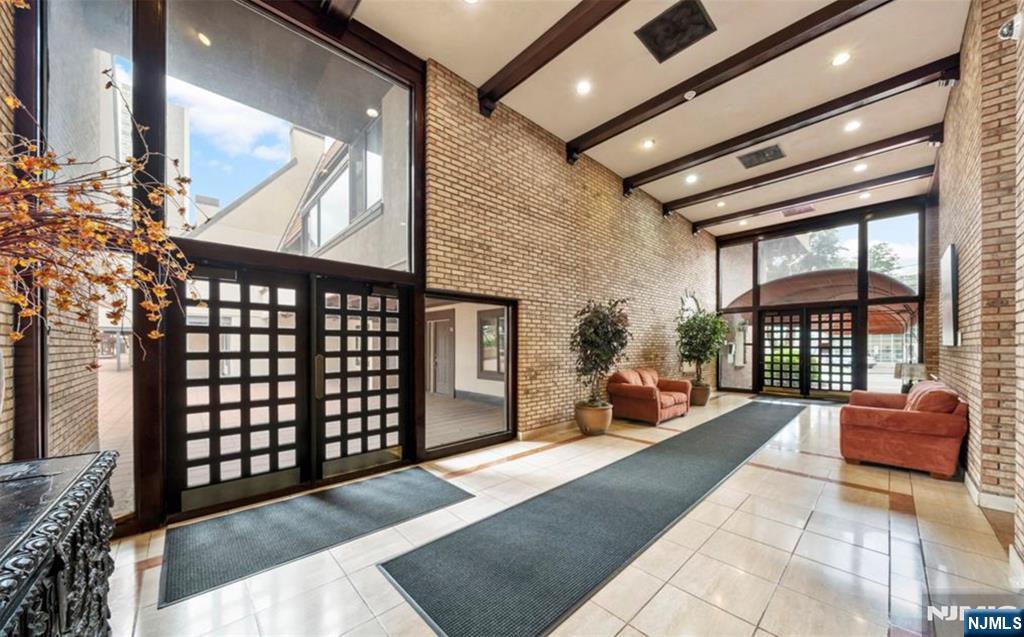 Condominium lobby with a high beamed ceiling, grid-pattern glass doors, and rust-colored sofas.