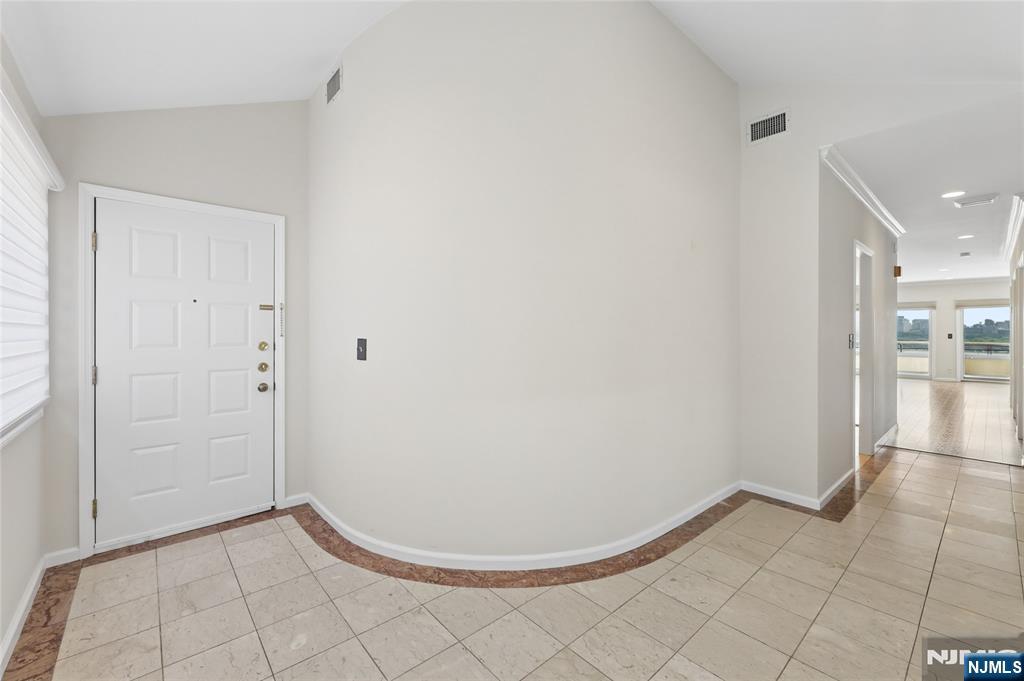 Apartment entry foyer with a white front door, curved wall, and tiled floor leading to a bright room.