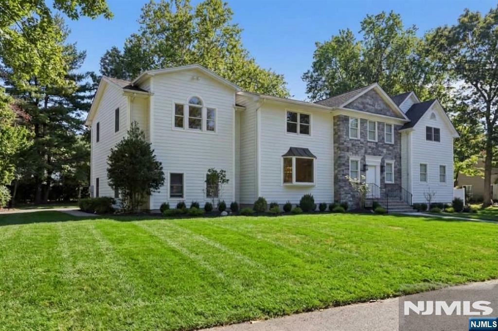 Large white two-story home with a stone entry, mature trees, and a broad green lawn.