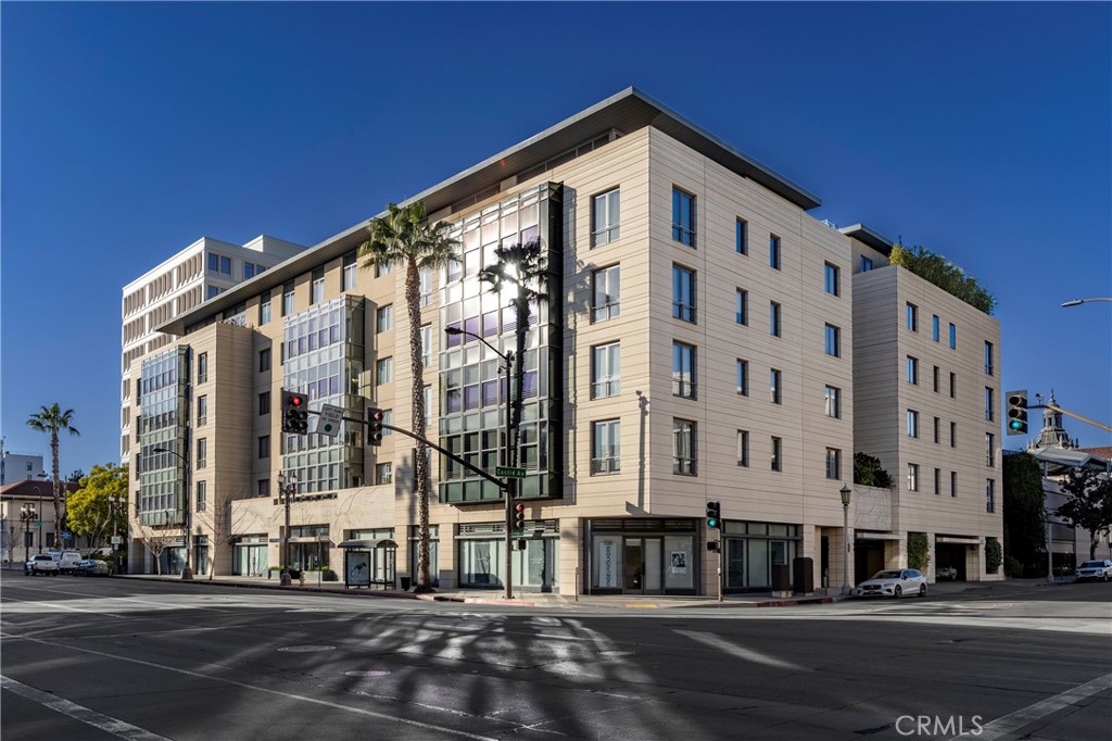 Modern beige multi-story building on a city corner, with glass windows and palm trees.